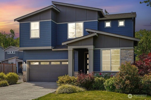 contemporary house featuring an attached garage, driveway, stone siding, fence, and board and batten siding