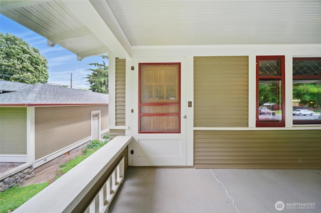 view of exterior entry with a shingled roof and a balcony