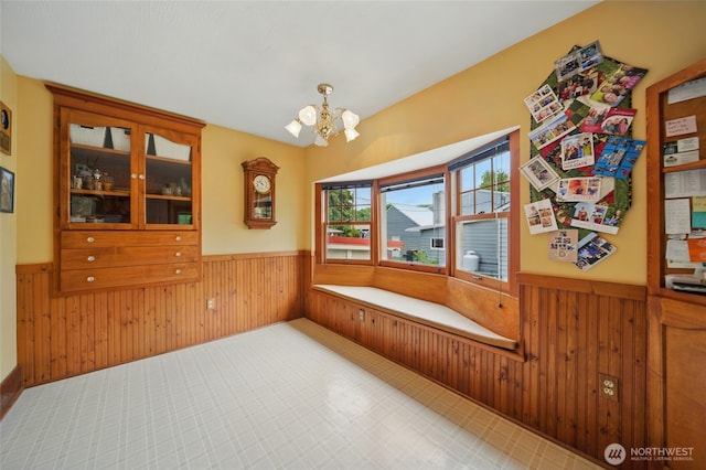 unfurnished dining area featuring a wainscoted wall, wooden walls, and a chandelier