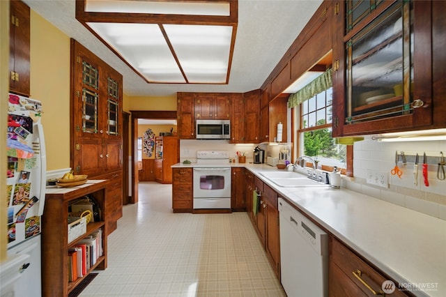 kitchen with white appliances, a sink, light countertops, and glass insert cabinets