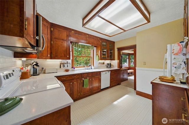 kitchen featuring white appliances, a sink, plenty of natural light, light countertops, and wainscoting