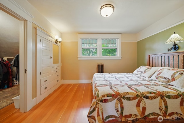 bedroom with radiator, light wood-type flooring, and baseboards