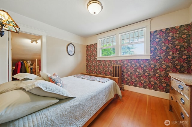bedroom featuring radiator, baseboards, wallpapered walls, wood finished floors, and a spacious closet