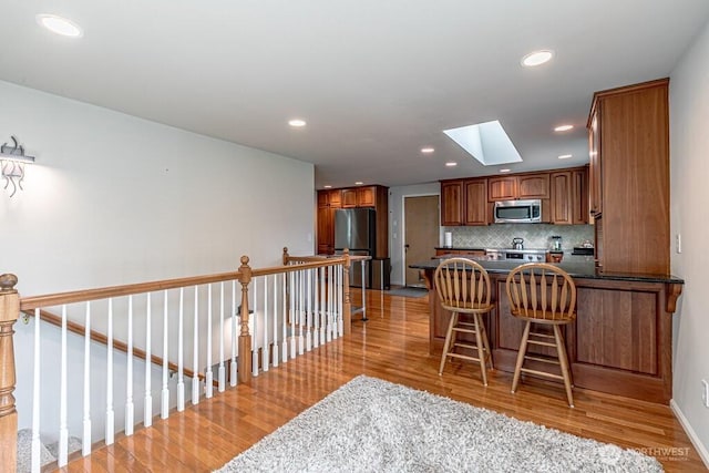 2117 130th Dr NE, Lake Stevens, WA 98258 - kitchen with stainless steel appliances, a skylight, light wood finished floors, dark countertops, and a peninsula