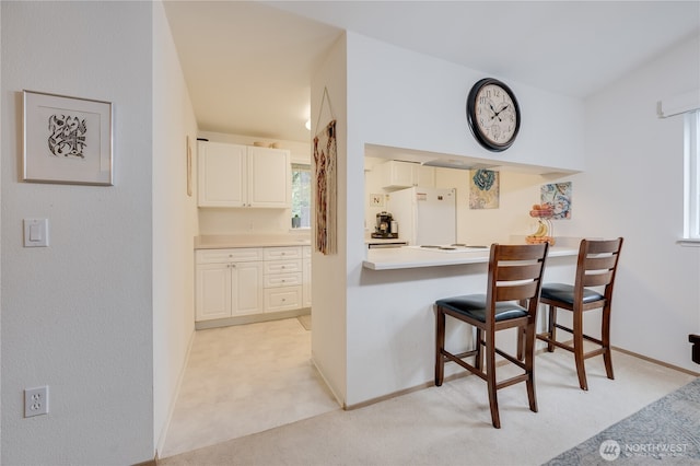 23313 Cedar Way Unit N205, Mountlake Terrace, WA 98043 - kitchen featuring freestanding refrigerator, a kitchen breakfast bar, baseboards, light countertops, and light colored carpet