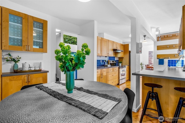 3527 E Spruce St, Seattle, WA 98122 - kitchen featuring electric stove, under cabinet range hood, dark countertops, a kitchen bar, and glass insert cabinets