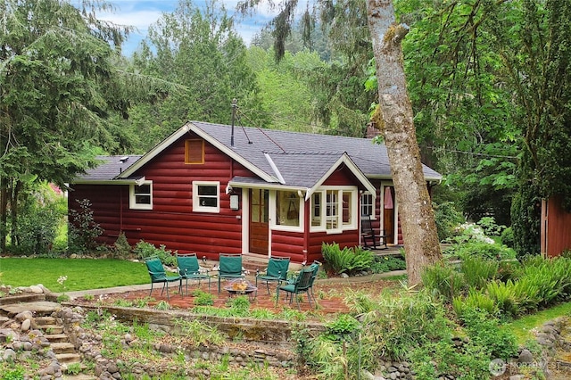 rear view of house with a shingled roof, faux log siding, a yard, and a view of trees