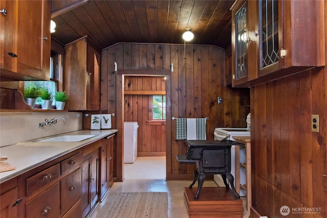 kitchen with a sink, wooden walls, washer / dryer, wooden ceiling, and light countertops