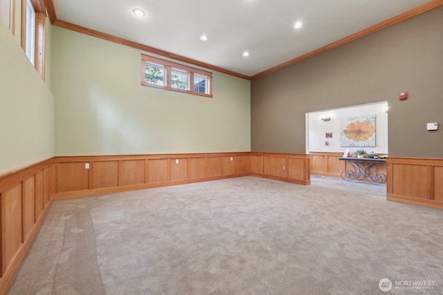 spare room featuring ornamental molding, light colored carpet, wainscoting, recessed lighting, and a decorative wall