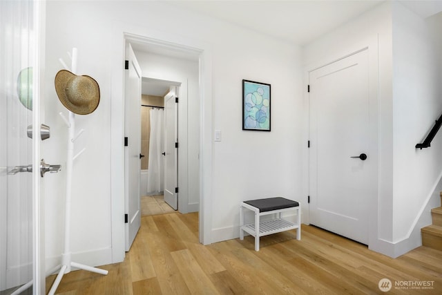 hallway featuring light wood-style flooring, baseboards, and stairway
