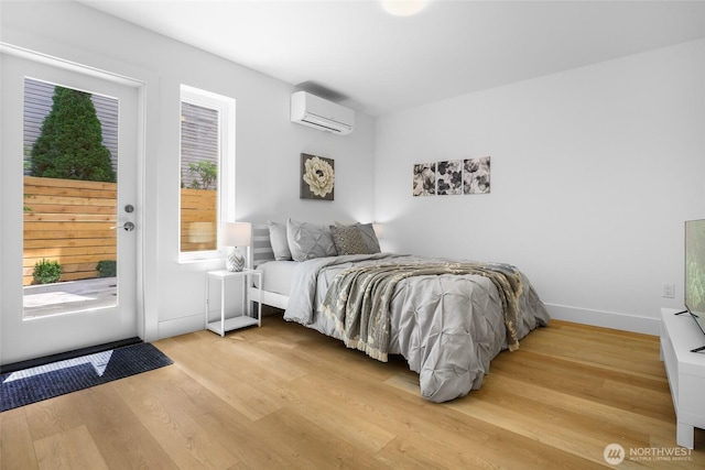 bedroom with a wall mounted air conditioner, access to outside, light wood finished floors, and baseboards