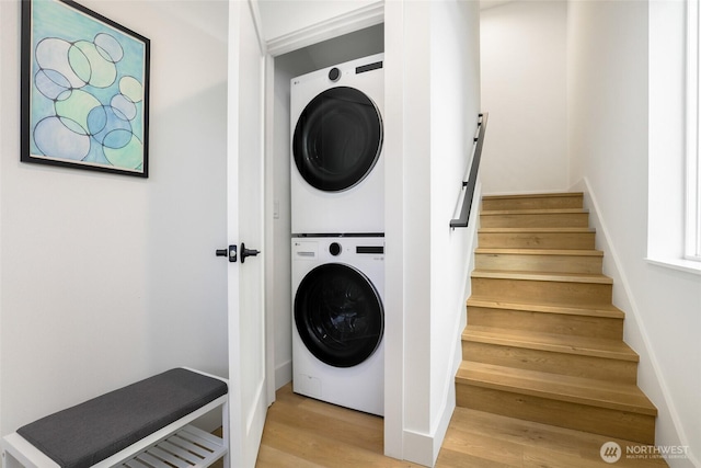 laundry area featuring stacked washer and clothes dryer, light wood-type flooring, and baseboards