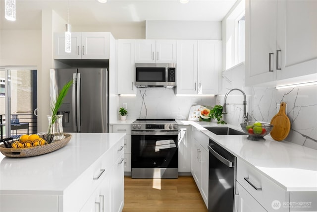kitchen with appliances with stainless steel finishes, a sink, light wood-style floors, backsplash, and light countertops