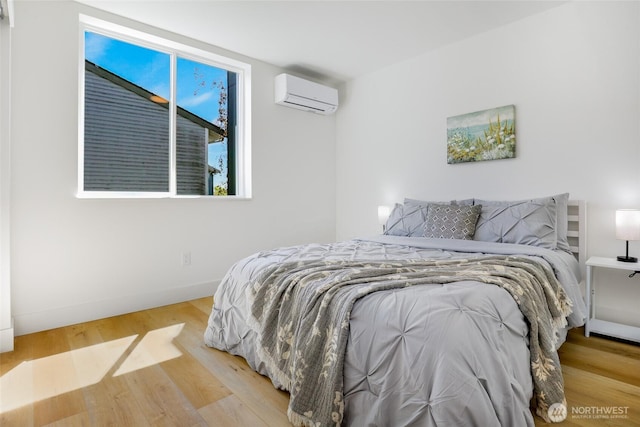 bedroom featuring a wall mounted AC, wood finished floors, and baseboards