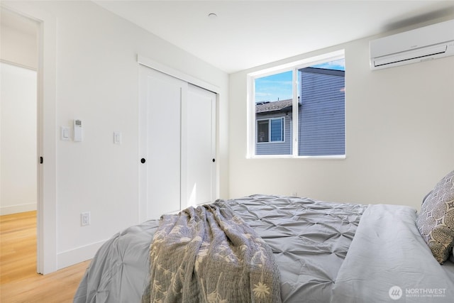 bedroom with a wall unit AC, wood finished floors, baseboards, and a closet