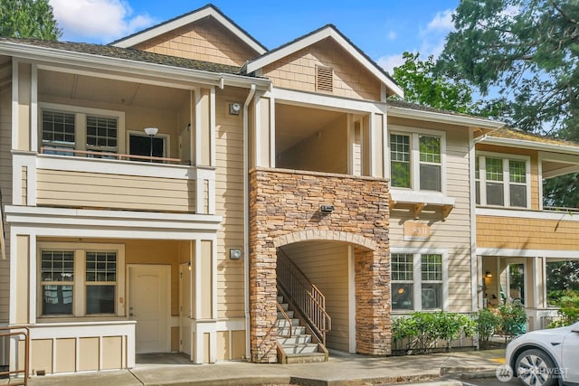 view of front of house featuring stone siding, a balcony, and stairs