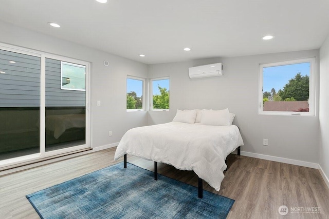 bedroom with a wall mounted air conditioner, baseboards, wood finished floors, and recessed lighting