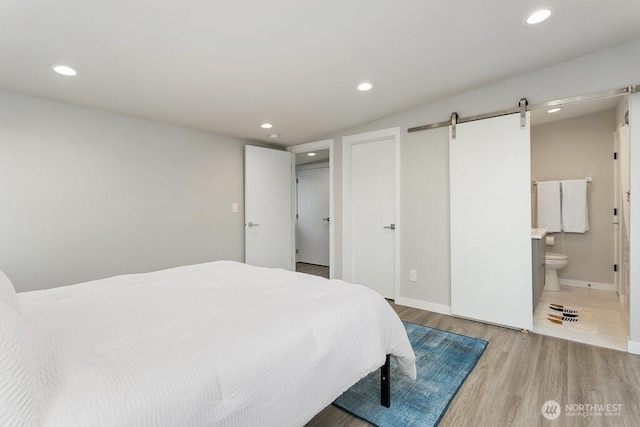 bedroom featuring wood finished floors, a barn door, recessed lighting, baseboards, and ensuite bathroom