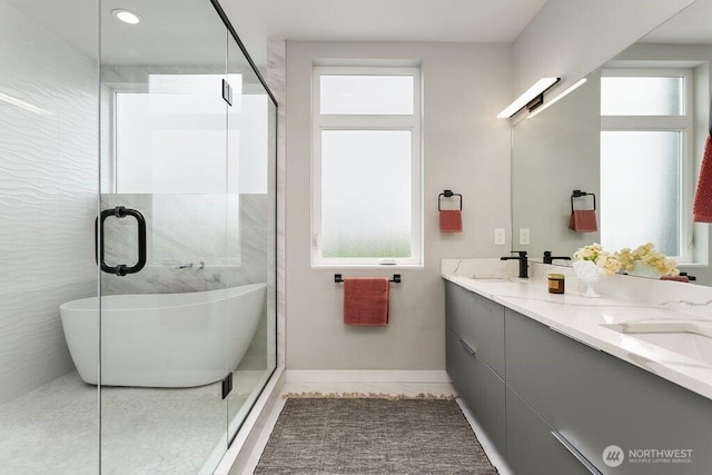 full bath featuring healthy amount of natural light, double vanity, a shower with shower door, and baseboards