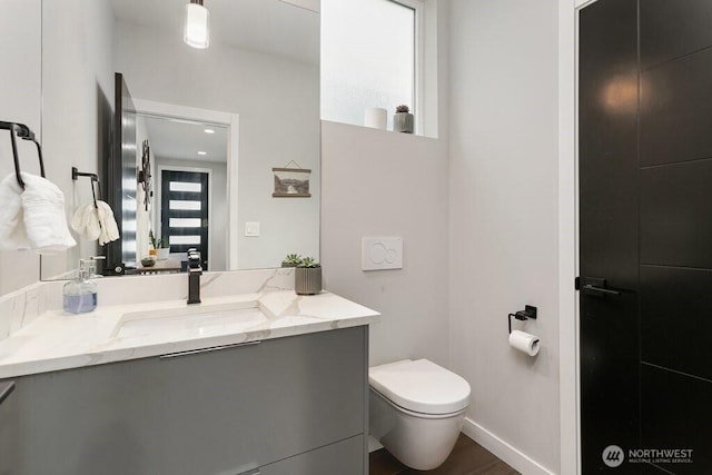 bathroom with toilet, vanity, wood finished floors, and baseboards