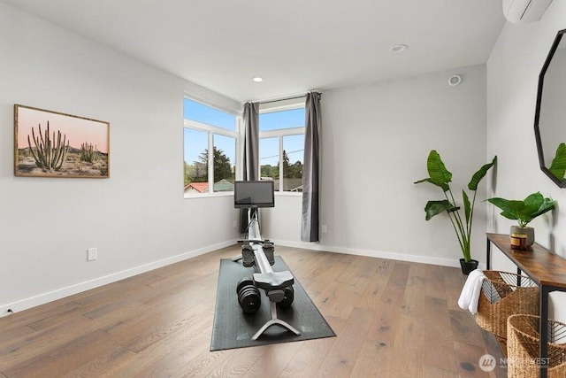 exercise room featuring a wall unit AC, baseboards, wood finished floors, and recessed lighting