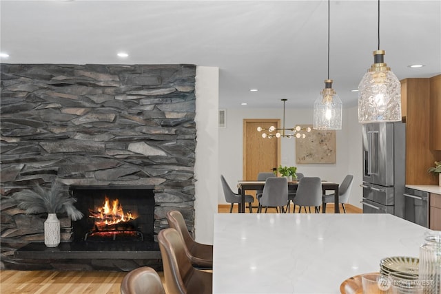dining area featuring wood finished floors, a chandelier, a stone fireplace, and recessed lighting