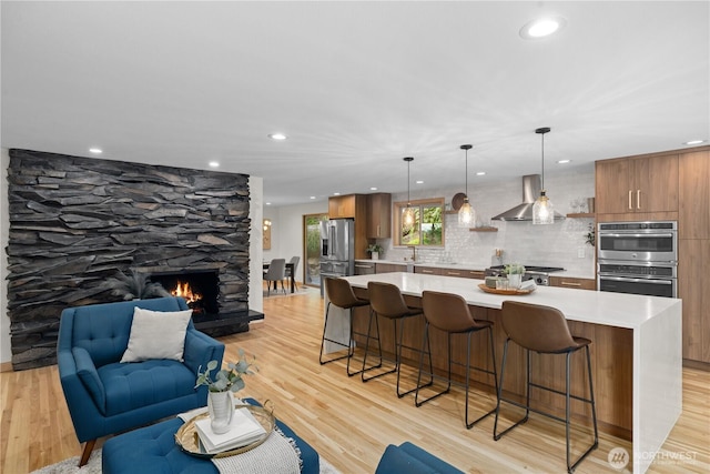 kitchen with appliances with stainless steel finishes, a breakfast bar area, light countertops, wall chimney exhaust hood, and light wood-style floors