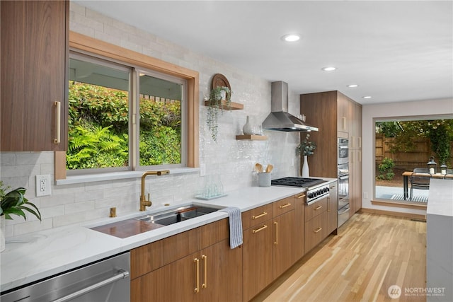 kitchen with wall chimney exhaust hood, a sink, appliances with stainless steel finishes, backsplash, and light wood-style floors