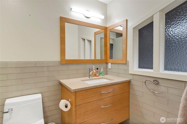 bathroom with tile walls, vanity, toilet, and wainscoting
