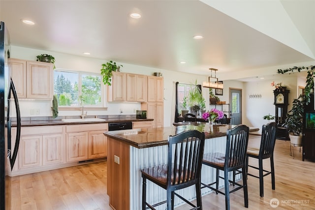 kitchen with light brown cabinets, a breakfast bar area, dark countertops, black appliances, and recessed lighting
