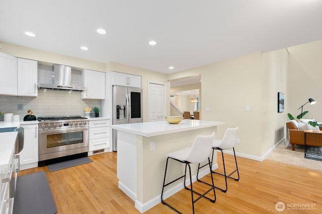23322 SE 26th Pl, Sammamish, WA 98075 - kitchen with wall chimney range hood, appliances with stainless steel finishes, a breakfast bar area, white cabinets, and recessed lighting