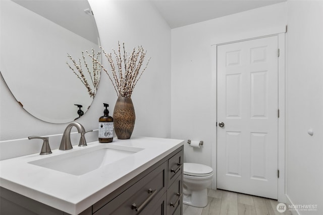bathroom with toilet, vanity, and wood finished floors