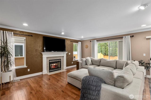 living area featuring crown molding, hardwood / wood-style flooring, a tiled fireplace, baseboards, and recessed lighting