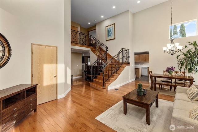 living room featuring a towering ceiling, a chandelier, stairway, hardwood / wood-style flooring, and baseboards