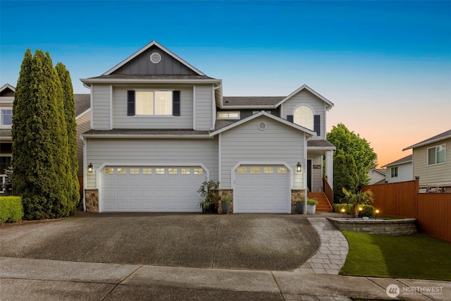 view of front of house with driveway, stone siding, board and batten siding, fence, and a garage
