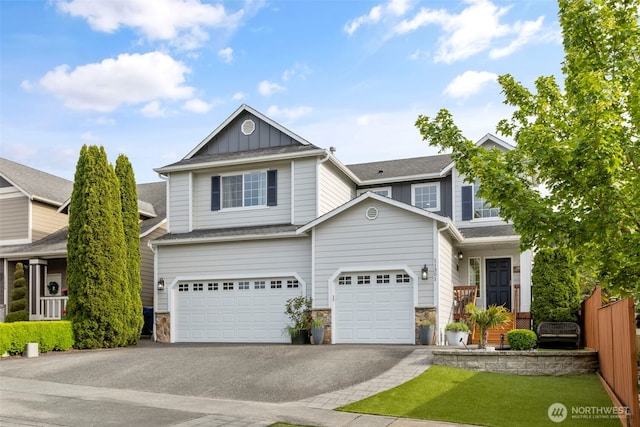 view of front of property with asphalt driveway, board and batten siding, stone siding, fence, and an attached garage