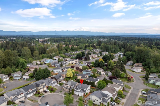 aerial view of property's location featuring nearby suburban area, a mountain backdrop, and a heavily wooded area