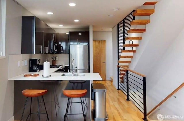 kitchen featuring a sink, a peninsula, appliances with stainless steel finishes, light countertops, and a breakfast bar