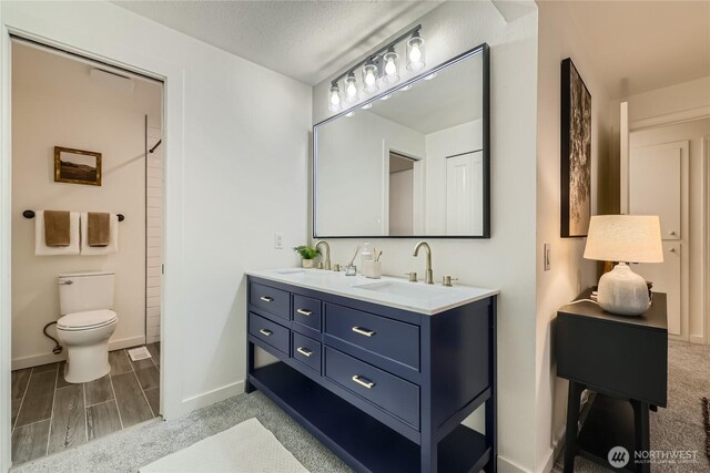 bathroom with toilet, double vanity, baseboards, and a shower