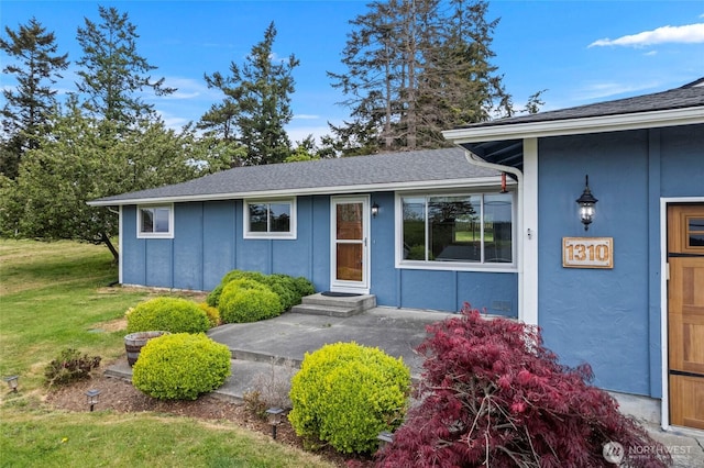 view of front of home featuring a front yard, roof with shingles, and stucco siding