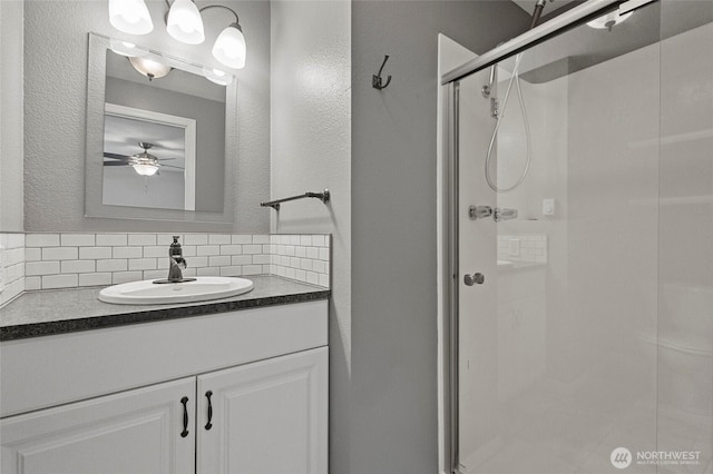 full bath with backsplash, a shower stall, a ceiling fan, vanity, and a textured wall