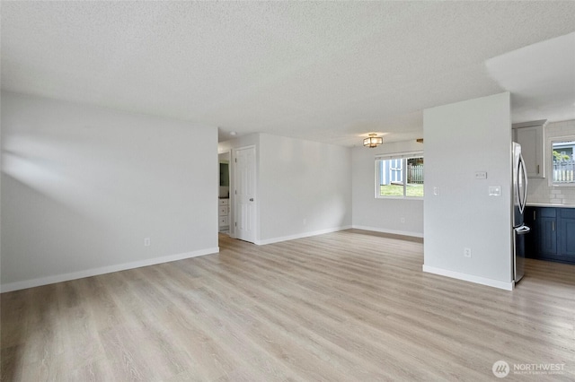 unfurnished living room with light wood-type flooring, a textured ceiling, plenty of natural light, and baseboards