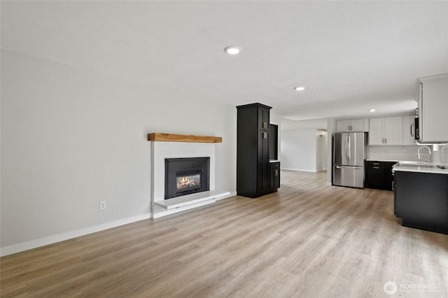 unfurnished living room with light wood finished floors, recessed lighting, baseboards, and a glass covered fireplace