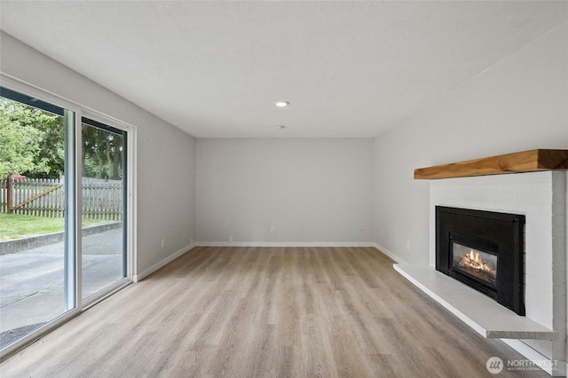 unfurnished living room featuring light wood finished floors, a glass covered fireplace, baseboards, and recessed lighting