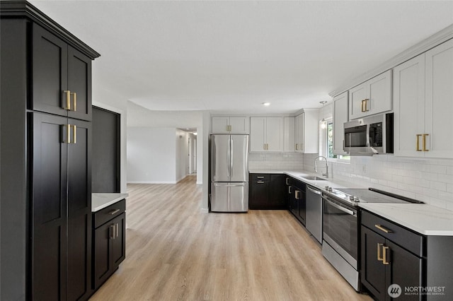 kitchen with stainless steel appliances, a sink, light wood-style flooring, decorative backsplash, and dark cabinets