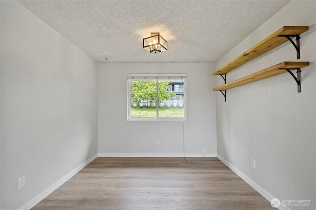 unfurnished room featuring a textured ceiling, light wood finished floors, and baseboards