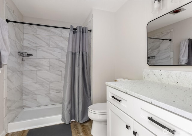 full bathroom with a tile shower, toilet, wood finished floors, and vanity