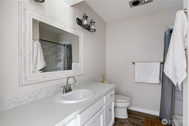 bathroom with wood finished floors, vanity, toilet, backsplash, and baseboards