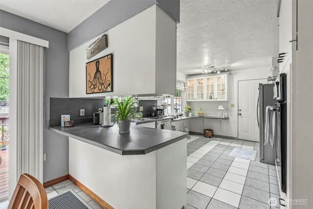 kitchen with a peninsula, light tile patterned floors, dark countertops, a textured ceiling, and baseboards