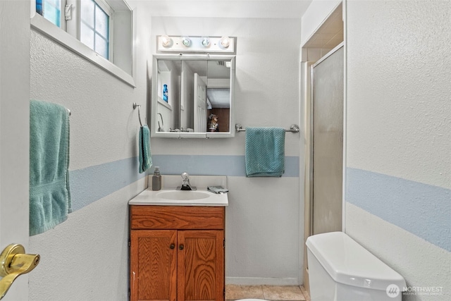 full bath featuring a shower stall, vanity, a textured wall, toilet, and tile patterned flooring